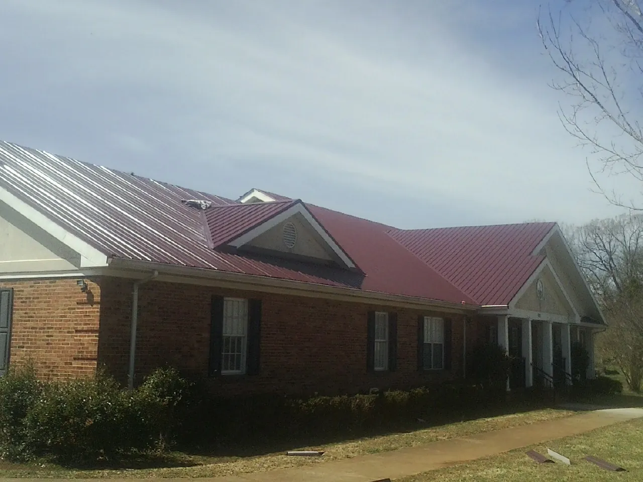 Red metal roof with gabled entries on a long brick building, from a Hail Damage Roof Repair job in Downingtown