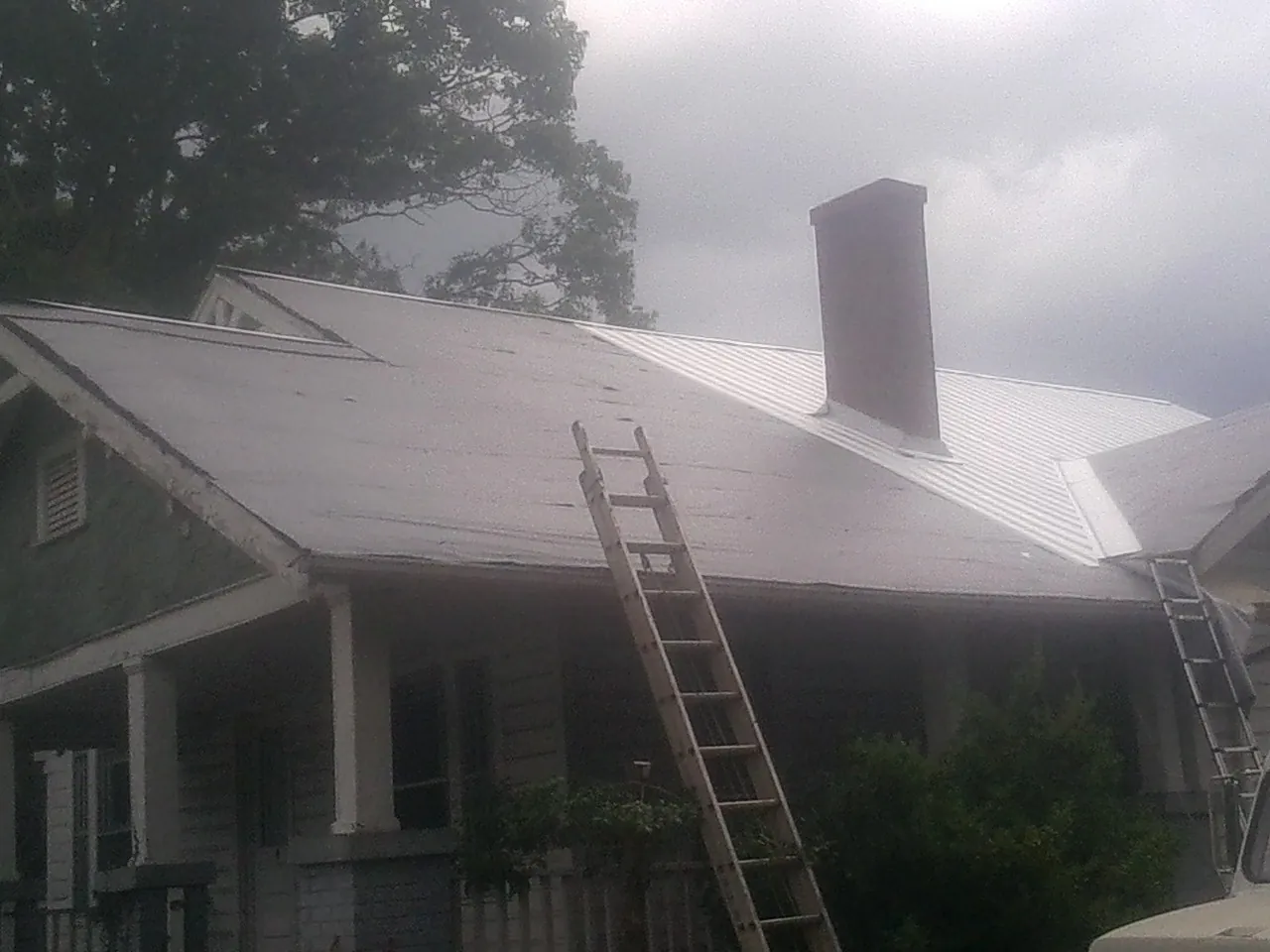 Ladders against a metal roof on an older home with a brick chimney in Downingtown