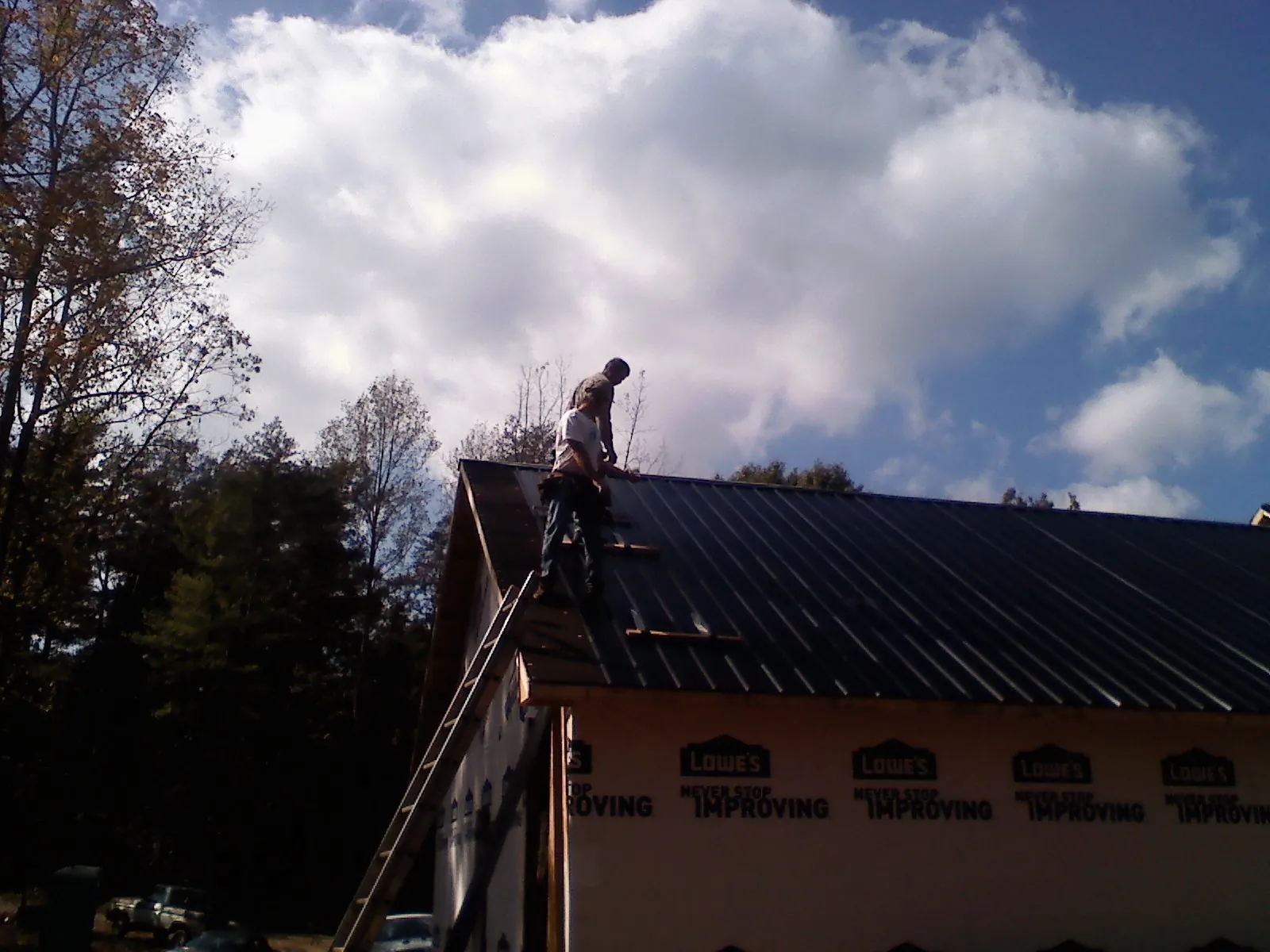 Roofer fastening dark metal panels high against a cloudy sky, from a Roof Inspection job in Downingtown