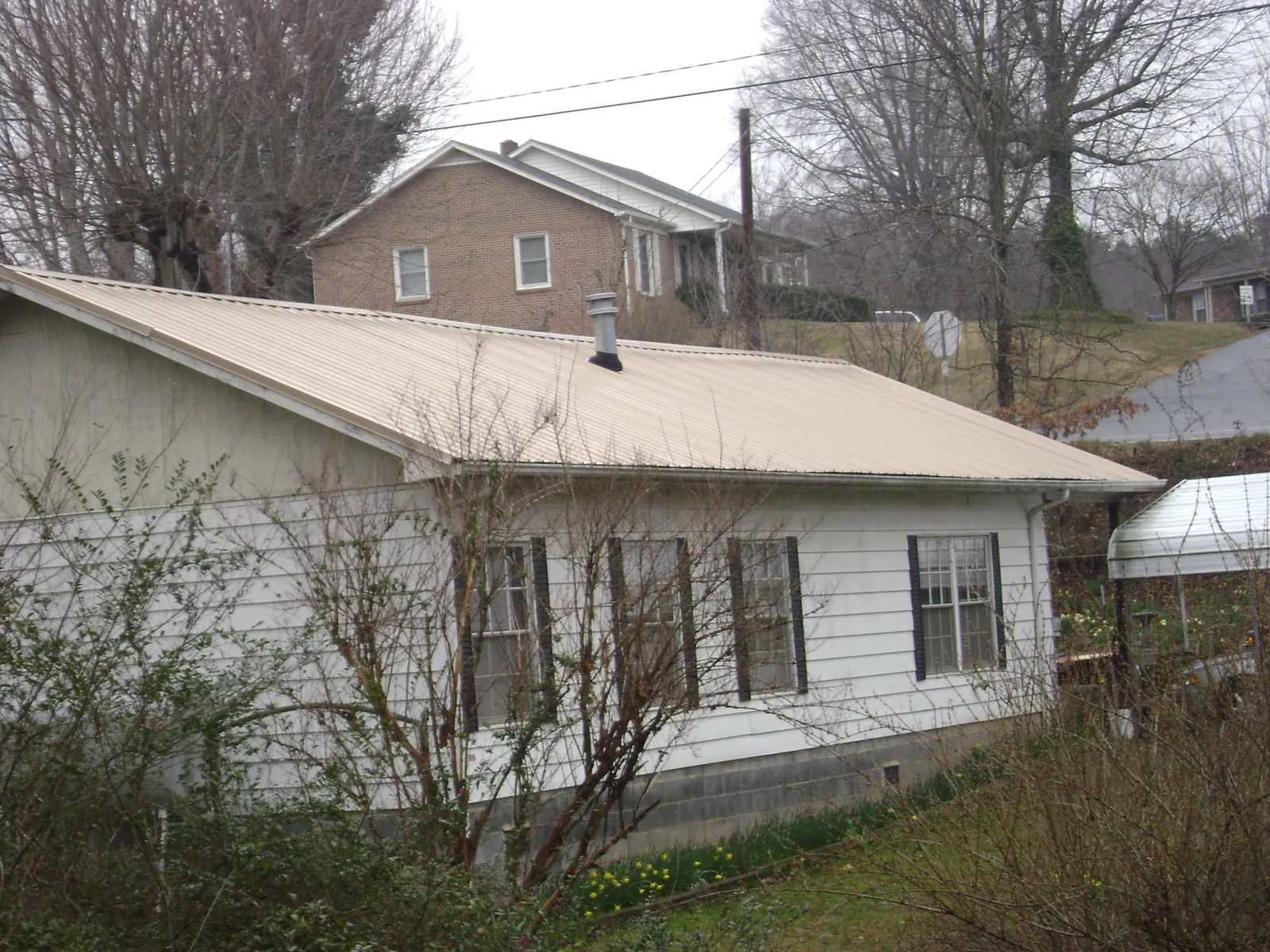 Tan metal roof on a white sided house set into a hillside — Commercial Roofing by Roofing Brothers in Downingtown